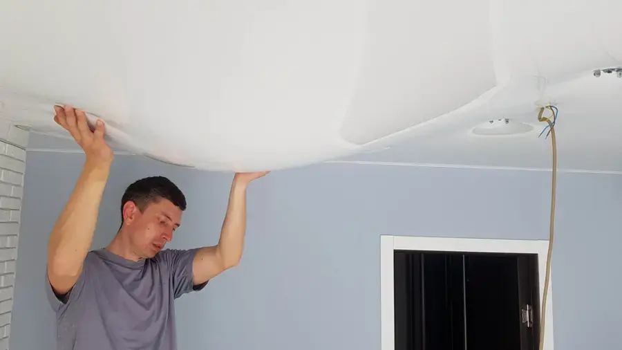 Homeowner pressing on a ceiling sagging with trapped water from a leak above in Blue Springs