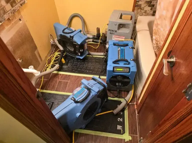 Air movers and dehumidifiers drying the floor and walls of a small room during structural drying in Blue Springs